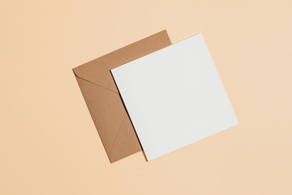A minimalist flat lay of a brown envelope with a blank card on a pastel background.